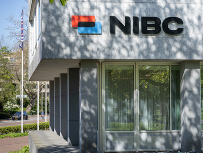NIBC-kantoor met rood en blauw logo op een moderne gevel, omringd door groene bomen.