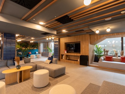 Moderne lounge met gezellige zithoeken, planten en een grote televisie op een houten wand.