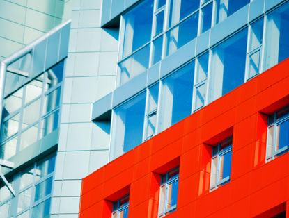 Close-up van een modern gebouw met blauwe en rode gevels; de rode muur heeft grote ramen die de architectonische lijnen benadrukken.