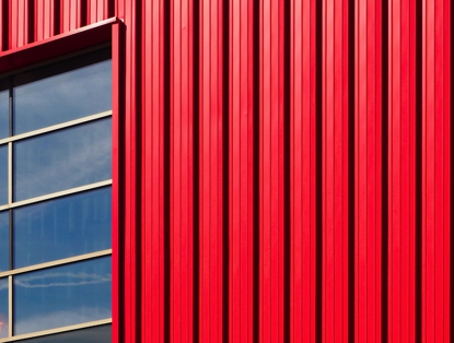 Rode metalen wand met een groot raam dat de blauwe lucht weerspiegelt.