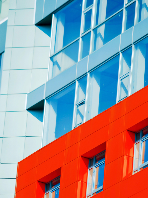 Detail van een gebouw met een felrode gevel en veel glas, wat de moderne architectuur benadrukt.