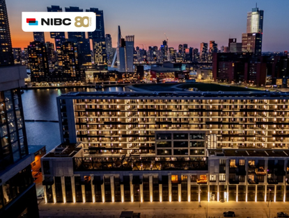 Stadsgezicht van een verlichte skyline met moderne gebouwen en water, met het logo van NIBC 80 jaar bovenaan.