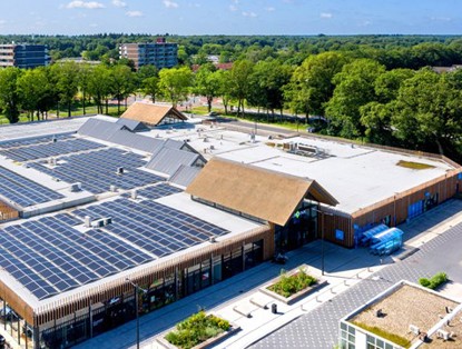 Luchtfoto van een modern, duurzaam gebouw met zonnepanelen op het dak en een groene omgeving.