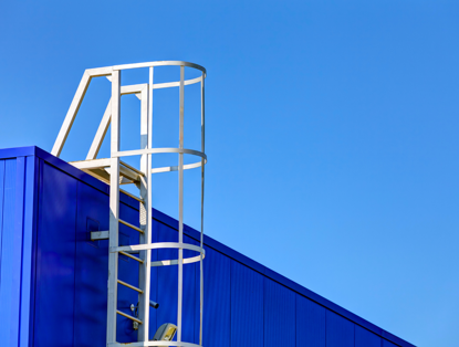 Witte ladder tegen een blauwe muur onder een heldere blauwe lucht.
