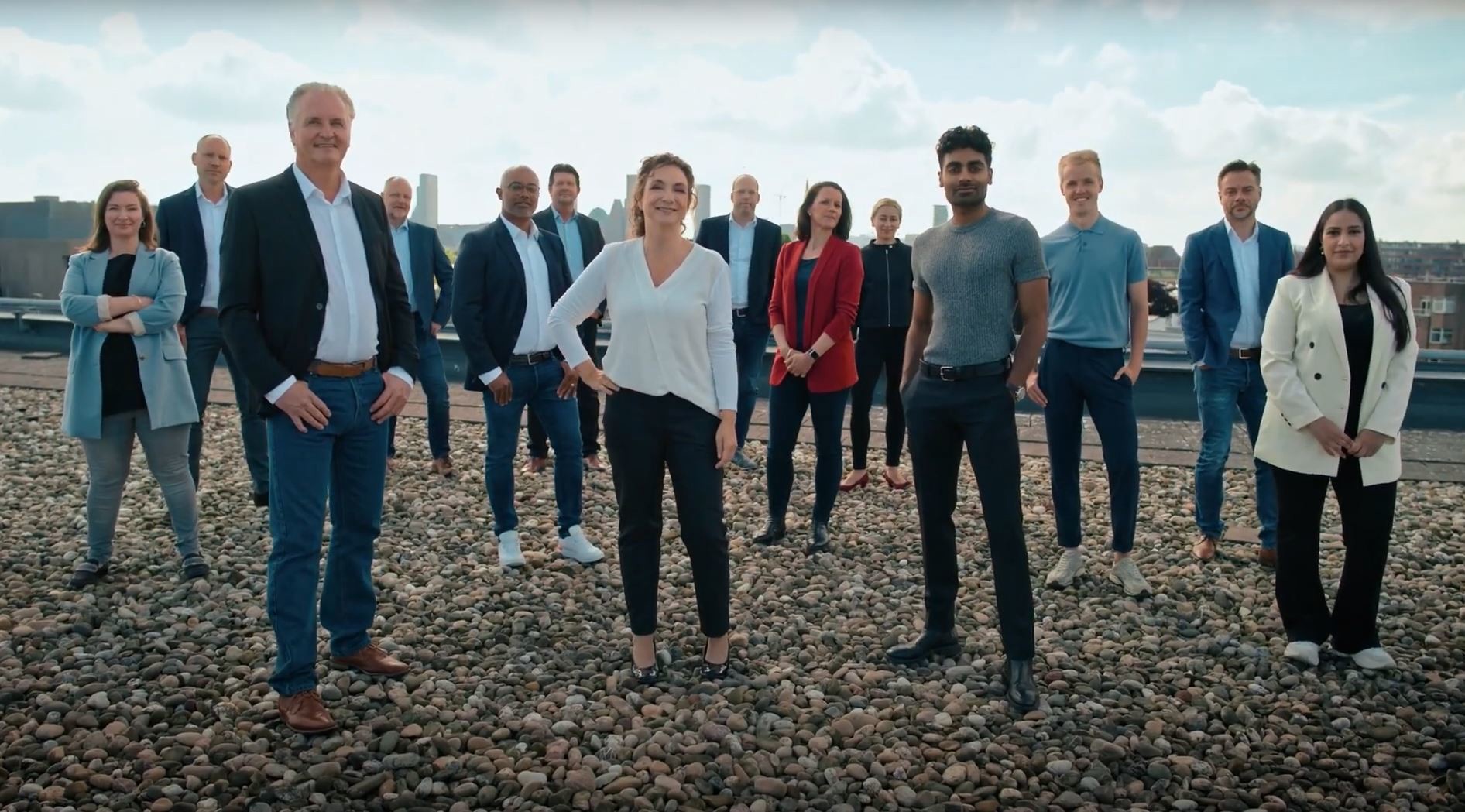 Groep professionals in formele en casual kleding poseren samen op een dakterras voor een teamfoto.