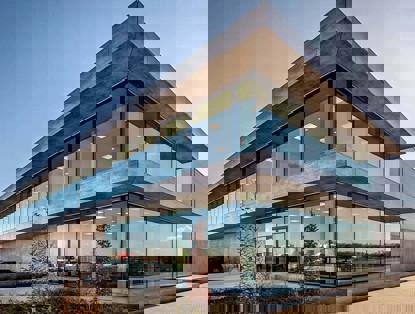 Modern kantoorgebouw met een glazen façade en betonnen elementen, omgeven door groen.